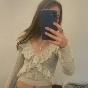 Beige stickad tröja med volangdetaljer - Säljer en söt beige stickad tröja med volangdetaljer framtill. Tröjan är croppad och har långa ärmar, perfekt för en trendig look. Passar bra till både jeans och kjol!