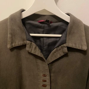 Grå kappa med knappar - Säljer en stilren grön kappa med urgulliga knappar framtill. Perfekt för höst och vår. Står strl M men är liten på mig med S