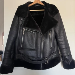 Svart skinnjacka med pälsfoder - Säljer en snygg svart skinnjacka med mjukt pälsfoder. Jackan har en bikerstil med flera dragkedjor och ett bälte i midjan. Perfekt för höst och vinter när du vill hålla dig varm och stilren. Lite större i storlek