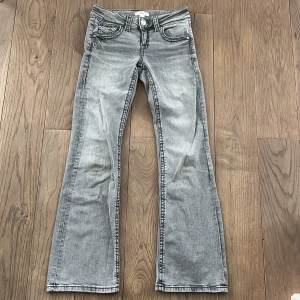 Grå bootcut jeans - Snygga grå bootcut jeans med klassisk femficksdesign och knappgylf. Perfekta för en avslappnad stil med en touch av retro. Passar bra till både sneakers och boots.