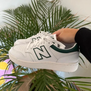 Vita sneakers från New Balance - Snygga vita sneakers från New Balance med gröna detaljer och klassisk snörning. Perfekta för en stilren look med en sportig touch.