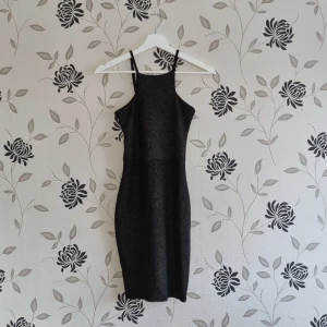Svart glittrig klänning från Nelly Trend, XS/34,  - Snygg svart glittrig klänning från Nelly med smala axelband och en figurnära passform. Perfekt för en kväll ute eller en speciell tillställning. Tillverkad i polyester med en touch av elastan för extra komfort.