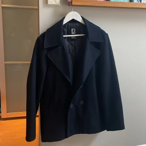 Svart skepparkavaj från Brandit - Snygg svart skepparkavaj från Brandit med dubbelknäppning och klassisk krage. Jackan har en quiltad insida för extra värme och stil. Perfekt för kyligare dagar. Storleken är M. Ändast använd vid 3 tillfällen. Saknar en knapp på högra sidan men inget man tänker på! Skriv vid funderingar!💫✨