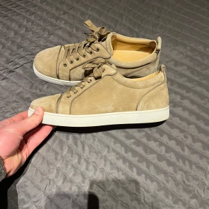 Christian Louboutin skor - Snygga beige sneakers i mocka från Christian Louboutin med den ikoniska röda sulan. 