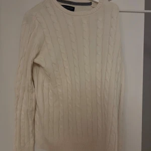 Vit stickad tröja Grisch - Säljer en stilren beige stickad tröja från Jack and Jones med klassiskt flätmönster. Tröjan har långa ärmar och ribbade muddar vid ärmslut och nederkant. Perfekt för kyliga dagar! Passar grisch stilen!