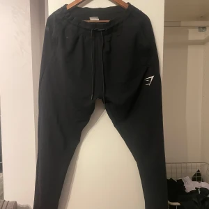 Svarta mjukisbyxor från Gymshark - Snygga svarta mjukisbyxor från Gymshark med en broderad logga på benet. Byxorna har en bekväm passform med snörning i midjan och är perfekta för träning eller avslappning.