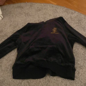 Svart hoodie från Juicy Couture - Snygg svart hoodie från Juicy Couture med guldtryck på bröstet och ryggen. Perfekt för en avslappnad stil med en touch av lyx. Mjuk och bekväm att bära.