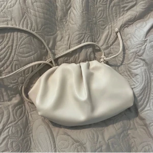 Vit axelväska - Snygg vit axelväska i syntetmaterial med en minimalistisk design. Väskan har en justerbar axelrem och en praktisk öppning.