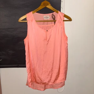 Rosa ärmlös topp från Holly & Whyte - Snygg rosa ärmlös topp från Holly & Whyte by Lindex. Toppen har en enkel design med en knappdetalj framtill och en luftig passform. Perfekt för varma sommardagar.