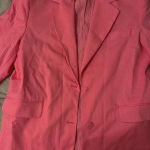 Rosa kavaj från Bershka - Snygg rosa kavaj från Bershka med klassisk design och knappar framtill. Perfekt för att liva upp garderoben med en färgklick. Tillverkad i ett bekvämt material som passar bra till olika tillfällen. Saknar en knapp. Använd en gång. Passar storlek 38-40 för oversize fit