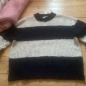 Randig stickad tröja från H&M - Säljer en mysig stickad tröja från H&M i svart och beige med breda ränder. Tröjan har långa ärmar och en klassisk passform, perfekt för kyligare dagar.