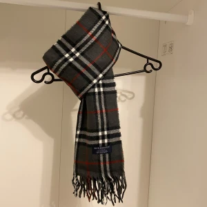 Burberry - Säljer nu denna Snygga halsduk från Burberry i färgen grå. Tillverkad i 100% mjuk kashmir med klassiskt fransad kant. Perfekt för att hålla dig varm och stilren under kyliga dagar. Hör av er vid funderingar☺️
