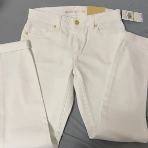 Vita skinny jeans från Michael Kors - Snygga vita skinny jeans från Michael Kors med guldfärgade knappar och detaljer. Perfekt för en stilren look. Dessa jeans har en klassisk femficksdesign och är tillverkade i ett bekvämt material.