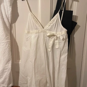 Vit klänning från Miss Sixty - Säljer en söt vit klänning från Miss Sixty med smala axelband och en dekorativ rosett i midjan. Klänningen har en v-ringad design och är perfekt för varma dagar.