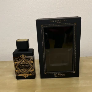 Oud for Glory Parfym 100ml - Elegant parfymflaska i svart med guldmönster från Badee Al Oud. Doften 'Oud for Glory' ger en lyxig och mystisk känsla. Flaskan har en fyrkantig form med en matchande svart kork. Perfekt för den som älskar orientaliska dofter. ((Vinter))