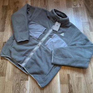 Nike ACG Polartec Arctic Wolf Fleece NY - Extremt cool gröngrå fleecejacka med flera fickor och en dragkedja framtill. Jackan har en logotyp på bröstet och en annan på ärmen. Storlek L men passar också M.