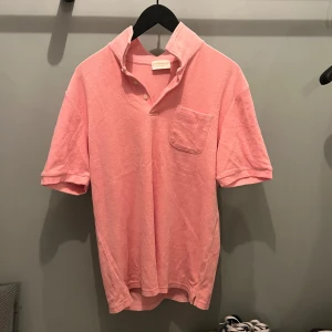 Rosa kortärmad pikétröja - Snygg rosa pikétröja med korta ärmar och en bröstficka. Perfekt för en avslappnad stil. Har en klassisk krage med knappar.