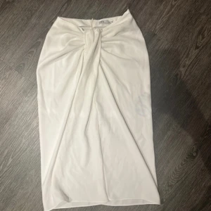 Vit kjol från Zara - Elegant vit långkjol från Zara med knytning framtill. Kjolen har en stilren design och en diskret dragkedja bak för enkel påklädning. Perfekt för en chic och sofistikerad look.