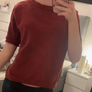 Vinröd stickad tröja - Säljer en vinröd stickad tröja med korta ärmar. Perfekt för en avslappnad stil. Tröjan har en enkel design med ribbade kanter vid ärmslut och nederkant.