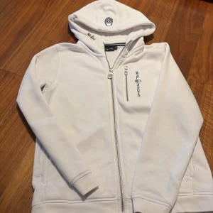 Vit hoodie från Sail Racing - Säljer en stilren vit hoodie från Sail Racing med dragkedja och logotyp på bröstet. 