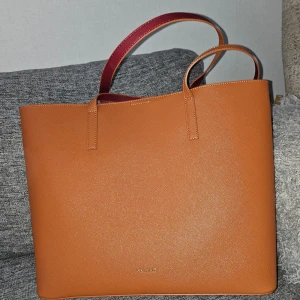 Orange shoppingväska från Anna Field - Snygg och rymlig orange shoppingväska från Anna Field med röda detaljer. Väskan har en praktisk dragkedja inuti och är perfekt för att bära med sig allt man behöver. Tillverkad i syntetmaterial med en stilren design.