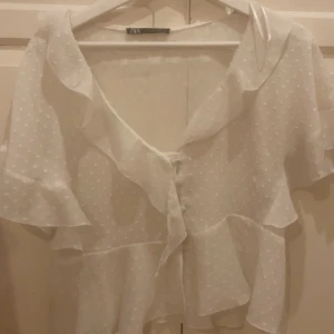 Vit blus från Zara - Söt vit blus från Zara med prickigt mönster och volangdetaljer. Blusen har korta ärmar och knytning framtill. Säljer då den inte kommer till mycket användning 💕