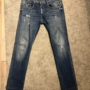 Blå jeans från Replay. Slitna - Säljer ett par snygga blå Replay Anbass jeans med slitna detaljer.  Skick 9/10. Storlek 34/31
