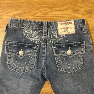 True Religion jeans - Snygga lågmidjade jeans från true religion dehär är joey modellen med detaljer och de säljs inte längre de kostade 1400kr nya och jag har använt dem 1 gång. Kan också byta dem mot vanliga true religion joey jeans i en ljus blå färg storlek 24/25. Säljer eftersom de inte har kommit i andvändning och är för små låten.