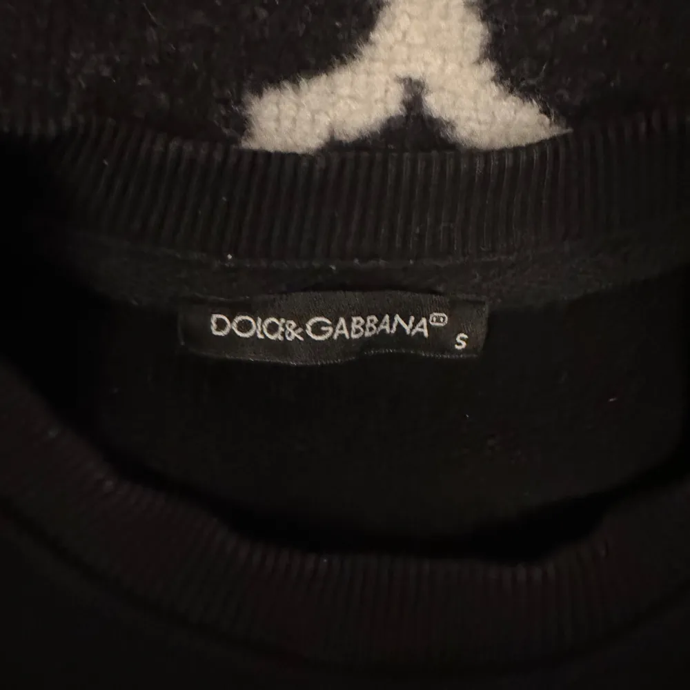 Snygg svart sweatshirt från Dolce & Gabbana med broderad logotyp och kransdetalj på framsidan. Tröjan har långa ärmar och en klassisk rund halsringning. Säljer då den blev för liten men den är riktigt fet!. Neuletakit & Villapaidat.