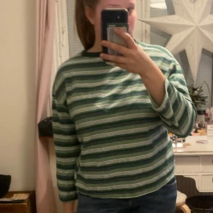 Grön- och vitrandig långärmad tröja - Säljer en grön- och vitrandig långärmad tröja med rund halsringning. Perfekt för en avslappnad stil. Tröjan har en bekväm passform och är lätt att matcha med jeans eller kjol. Storleken är S/M
