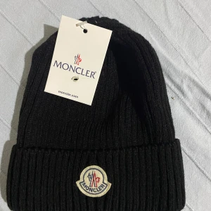 Svart  mössa från Moncler - Oanvänd monclears mössa. Snygg svart ribbad mössa från Moncler med broderad logotyp framtill. Perfekt för att hålla värmen under kyliga dagar. Stilren design som passar till det mesta.