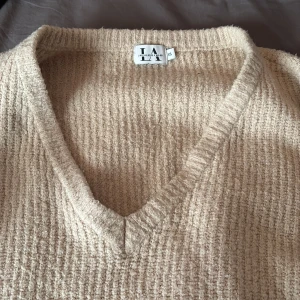 Beige stickad tröja från Linn Ahlborg x NA-KD - Mysig beige stickad tröja från Linn Ahlborg x NA-KD med v-ringning. Perfekt för kyligare dagar med sin mjuka och bekväma passform. Ett måste i garderoben för en stilren look.