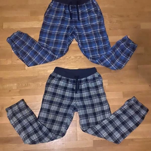Blå och grå rutiga mjukisbyxor - Två par mjukisbyxor i rutigt mönster. Ett par i mörkblått och ett i ljusgrått/ljusgrönt med elastisk midja och snörning. Perfekta för en avslappnad dag hemma. 60kr st eller 100kr för båda