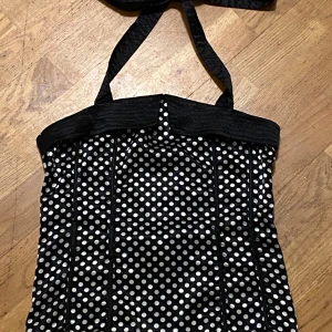 Svart prickig korsettopp!  - Snygg svart korsettopp med vita prickar och halterneckband. Toppen har en smickrande passform med dekorativa sömmar och en elastisk rygg för extra komfort. Perfekt för en kväll ute eller en speciell tillställning. Mycket fint skick! 