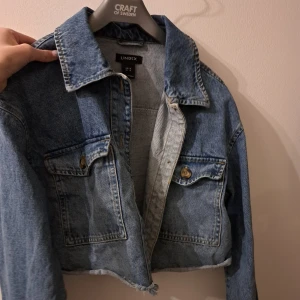 Blå jeansjacka - Säljer en snygg blå jeansjacka från Lindex. Jackan har en croppad design med två bröstfickor och knappar framtill. Perfekt för en avslappnad stil. Varan säljs inte längre på Lindex, den är S - M, men skulle nog säga att den är en S. 