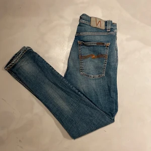 Nudie Jeans - Snygga blå jeans från Nudie Jeans i modellen Brute Knut. Jag har töjt ut jeansen i midjan så att de sitter som 27-28 i midjan. Tillverkade av 98% ekologisk bomull och 2% elastan för en bekväm passform. De har en klassisk femficksdesign och orange sömmar som ger en cool kontrast. Skriv vid minsta lilla fundering!✅🤝