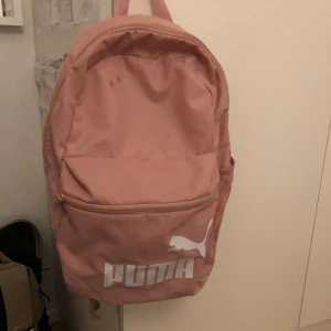 Rosa ryggsäck från Puma - Säljer en snygg rosa ryggsäck från Puma. Den har ett stort huvudfack och en praktisk framficka med dragkedja. Axelremmarna är justerbara för bästa komfort. Perfekt för skolan eller träningen!