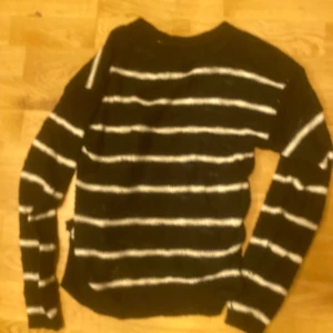 Svart och vit randig tröja - Säljer en svart tröja med vita ränder. Tröjan har långa ärmar och är perfekt för kyligare dagar. Den är både stilren och bekväm.