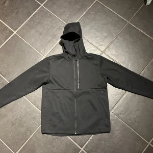 Svart siphoodie från H&M - Säljer en svart sportjacka från H&M med huva och dragkedja framtill. Jackan har långa ärmar och är perfekt för vardagsbruk. Enkel och stilren design som passar till det mesta.