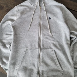 Grå hoodie med dragkedja från Ralph Lauren - Säljer en ralph lauren tröja då den hade fel passform för mig. Storlek M aldrig använd. Pris kan diskuteras, snabb på att svara och leverera