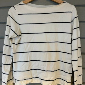 Vit och svart randig tröja från Uniqlo -  Tröja med marinblå ränder från Uniqlo. Tröjan har långa ärmar och en klassisk design som passar perfekt för en avslappnad look. Perfekt för dig som gillar enkel och tidlös stil. 