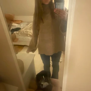 Beige stickad polotröja - Säljer en mysig beige stickad polotröja med hög krage. Tröjan har långa ärmar och en loose passform, perfekt för kyliga dagar. Den ribbade strukturen ger en stilren look. Passar utmärkt till både jeans och kjol.