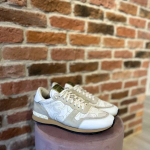 Valentino Rockrunner - Snygga beige sneakers med stjärnmönster och nitar på hälen. Skorna har en kombination av mocka och syntetmaterial med snörning framtill. Perfekta för en stilren look. Skorna är dessutom i ett extremt bra skick, inga tecken på användning.