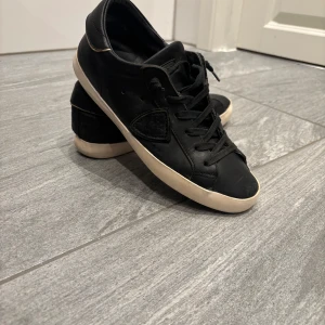 Svarta sneakers från Philippe Model - Snygga svarta sneakers från Philippe Model med klassisk design och vita sulor. Skorna har snörning och en diskret logga på sidan. Perfekta för en stilren look. Obs ingen box