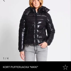 Kort svart pufferjacka 'Nikki' - Snygg och trendig kort svart pufferjacka med glansig yta och huva. Jackan har en dragkedja framtill och långa ärmar, perfekt för kyliga dagar. En stilren och modern look som passar till många outfits. Säljer för den inte kommer till användning. Använd en gång. Slut överallt. Pris kan diskuteras. Passar M