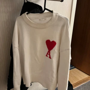 En vit ami Paris tröja men rött märke - Säljer en stilren vit ami Paris tröja med ett rött hjärta och bokstaven på bröstet. Tröjan har en rund halsringning och långa ärmar. Perfekt för en avslappnad look. Kvittot på denna har jag tappat bort men påse och mm finns kvar! Pris kan diskuteras!