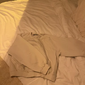 Beige sweatshirt från Bershka - Säljer en stilren beige sweatshirt från Bershka. Tröjan har en klassisk design med rund hals och ribbade muddar vid ärmslut och nederkant. Perfekt för en avslappnad look.