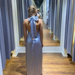 Ljusblå balklänning med rosett i ryggen  - Elegant ljusblå/silvrig långklänning med en stilren halterneck-design och rosett i nacken. Klänningen har en slits på sidan, perfekt för balen. Klänningen är helt ny. Köpte den till en fest som blev inställd. Storlek 36/S. Är från Lovisa Barkman kollektion med bikbok, helt slutsåld. Säljer för 1000kr då den är i nyskick. 