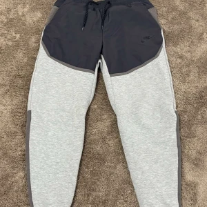 Grå och mörkgrå mjukisbyxor från Nike - Snygga mjukisbyxor från Nike i en kombination av ljusgrått och mörkgrått. Byxorna har en elastisk midja med snörning och praktiska fickor. Perfekta för en avslappnad stil.