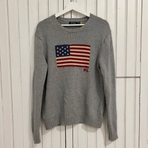 Ralph Lauren Stickad Tröja - Säljer denna eftertraktade Flag Sweater från Ralph Lauren.  Tröjan är i nyskick och är helt utan defekter. Storlek S.  Qr Scan medföljer för att garantera produktens autenticitet. Nypris på denna ligger på ca 6000kr, så här har du möjlighet till ett riktigt kap!